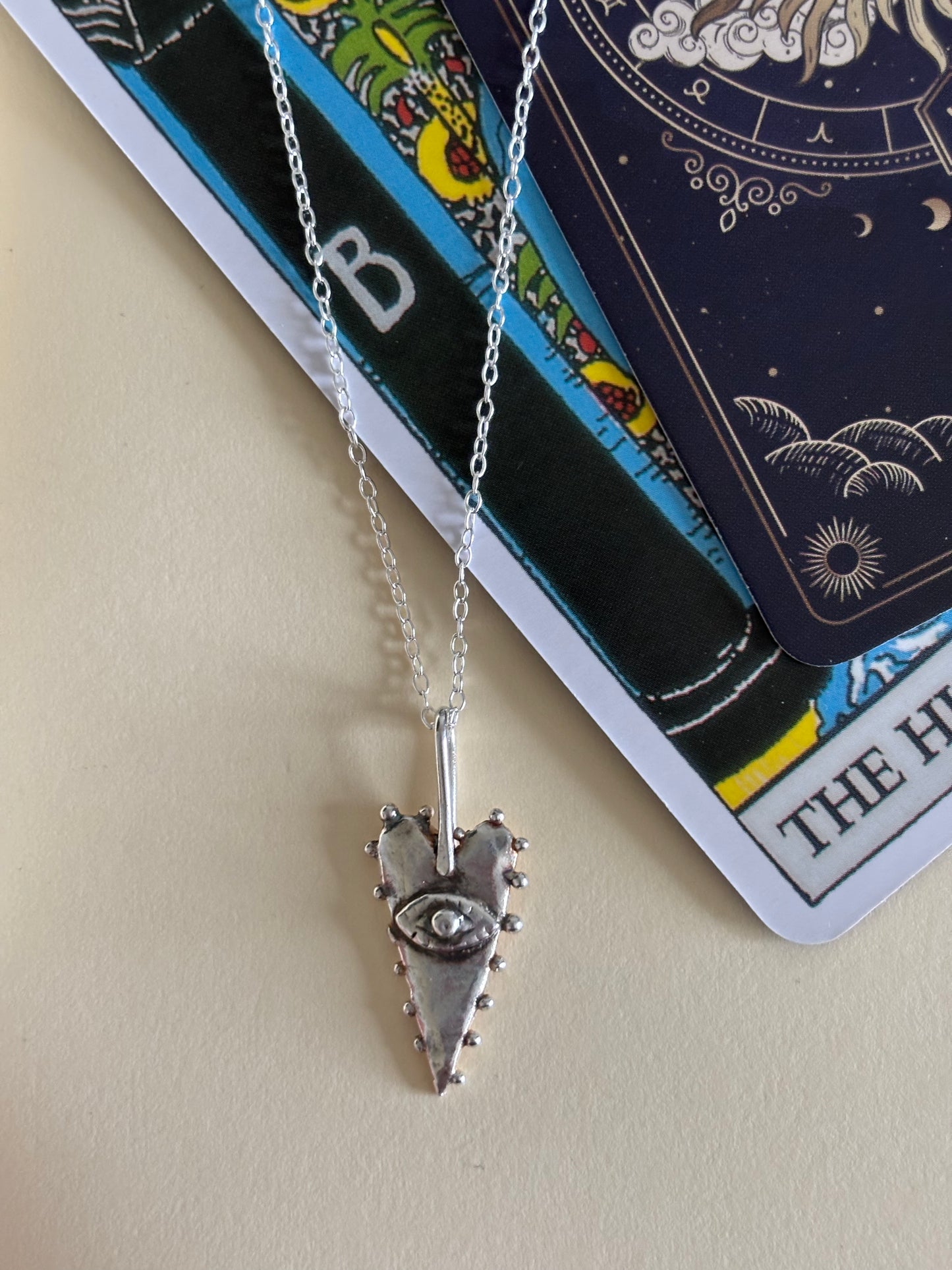 The All-Seeing Heart mystical silver tarot-inspired pendant photographed with tarot cards, highlighting its magical symbolism and divination-inspired aesthetic. Silver heart talisman featuring an all-seeing eye, representing intuition and inner vision. Artistic symbolic jewellery inspired by tarot, alchemy, magic, mystical traditions and esoteric imagery.
