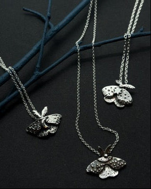 3 moth pendants on black background. Handcrafted silver moth pendant with detailed wings, inspired by nocturnal nature and made in Ireland. 
