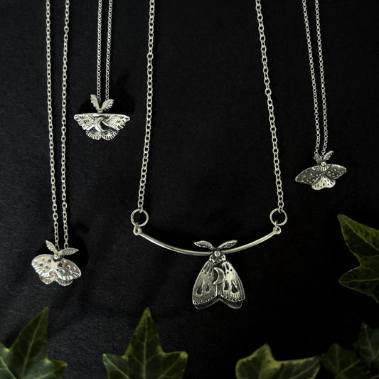 4 moth pendants on black background. Handcrafted silver moth pendant with detailed wings, inspired by nocturnal nature and made in Ireland by Irish jewellery designer