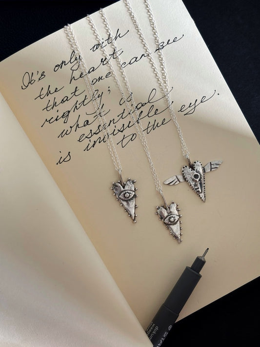 The All-Seeing Heart mystical silver pendant photographed on a notebook with the handwritten Little Prince quote, “It is only with the heart that one can see rightly; what is essential is invisible to the eye.” Tarot-inspired symbolic jewellery featuring an all-seeing eye and heart motif, inspired by magic, alchemy, intuition and hidden wisdom. Artistic silver talisman necklace with a whimsical, slightly naive aesthetic.
