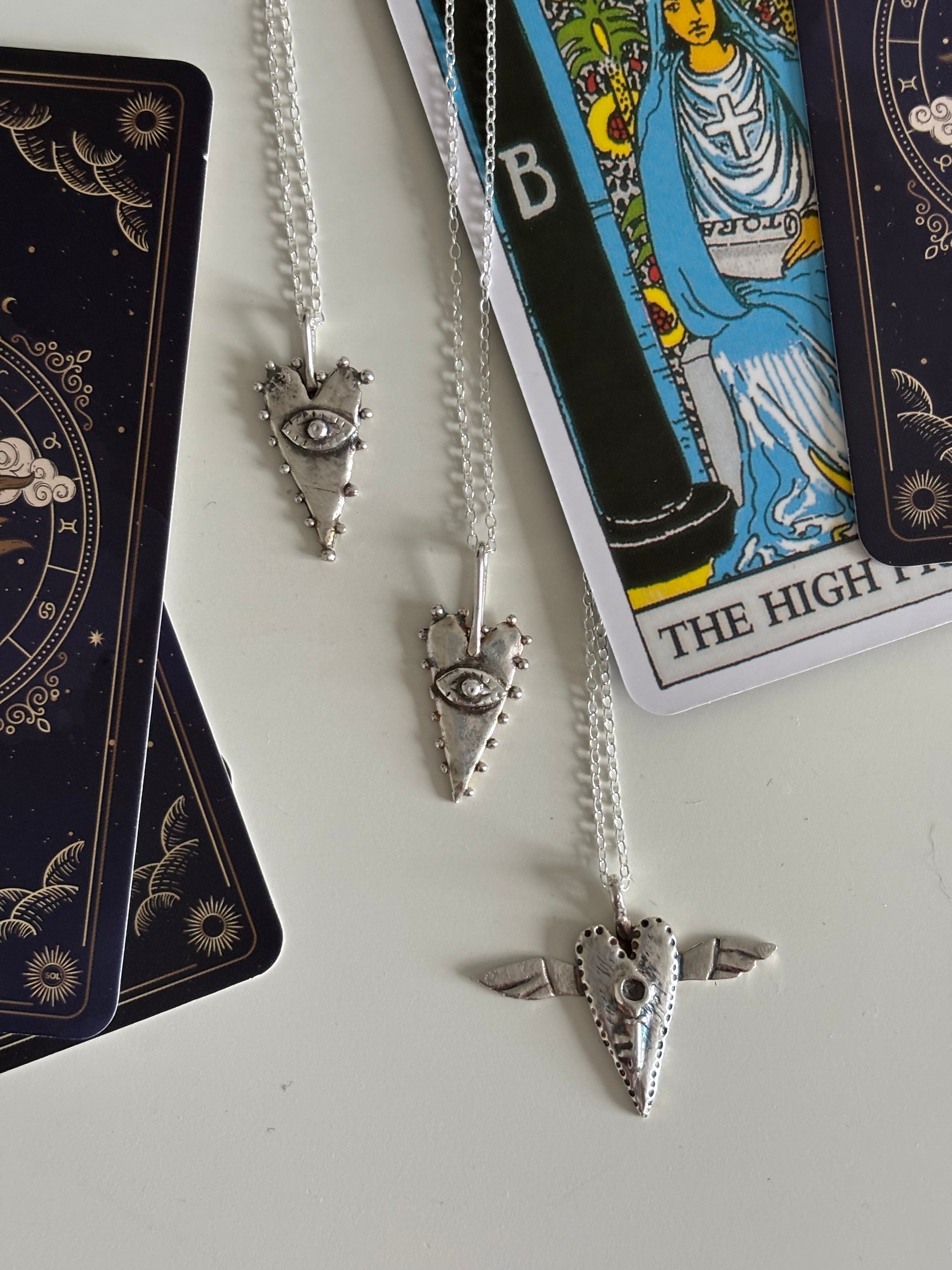 The All-Seeing Heart mystical silver tarot-inspired pendant photographed with tarot cards, highlighting its magical symbolism and divination-inspired aesthetic. Silver heart talisman featuring an all-seeing eye, representing intuition and inner vision. Artistic symbolic jewellery inspired by tarot, alchemy, magic, mystical traditions and esoteric imagery.