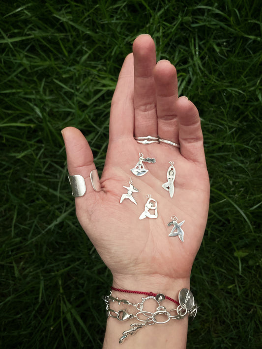 Five handmade sterling silver yoga pose pendants resting in the palm of a hand, showing the full collection together. Each pendant is hand-cut from sterling silver sheet in a loose doodle-style design, featuring a different yoga pose with simple, flowing lines. The scale of the pendants is shown against the hand, highlighting their lightweight, delicate feel and handmade character. Sustainable handmade Irish jewellery by an Irish jewellery designer, inspired by yoga, movement and mindful living.